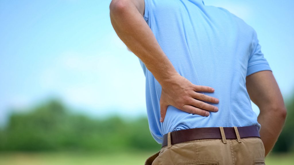 man feeling lower back pain radiating down legs - sciatica