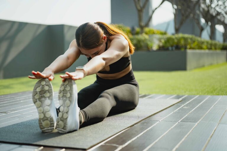 Active woman performing seated forward stretch yoga mat outdoors, improving flexibility, mobility recovery, and overall wellness healthy lifestyle setting